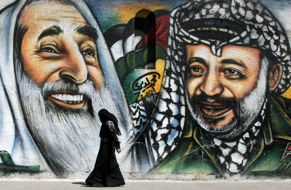 A Palestinian woman walks past a mural depicting late Palestinian leader Yasser Arafat, right, and late Hamas spiritual leader Sheikh Ahmed Yassin, left.