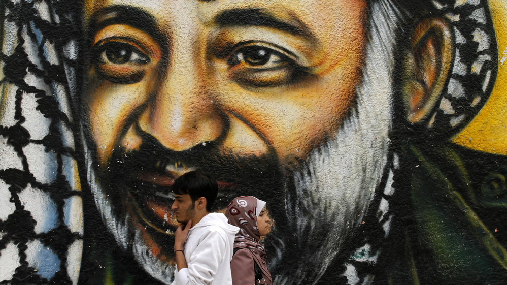 Palestinians walking in front of a mural of late Palestinian leader Yasser Arafat in Gaza City earlier today.