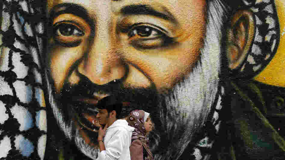 Palestinians walking in front of a mural of late Palestinian leader Yasser Arafat in Gaza City earlier today.