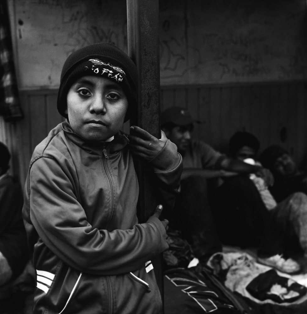 A 9-year-old Guatemalan boy traveling with his mother waits for a train with other migrants seeking shelter from the elements under the tin roof of a concession stand near the tracks in Orizaba. July 2010.