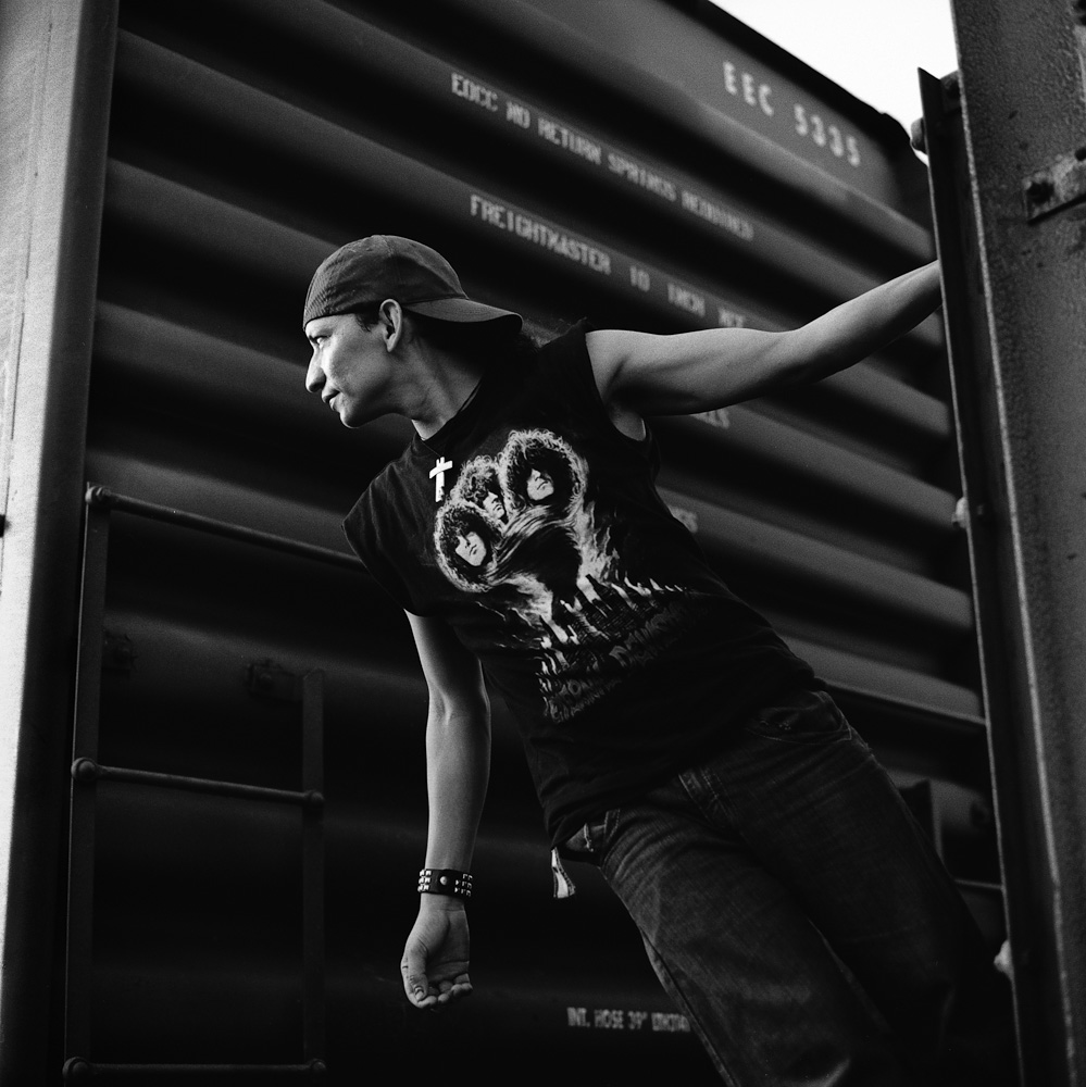 A Salvadoran migrant hangs onto a rail between two boxcars in a rail yard. Some travel approximately 150 miles by foot to Arriaga in Chiapas, Mexico, in order to avoid Mexican immigration checkpoints. July 2010.