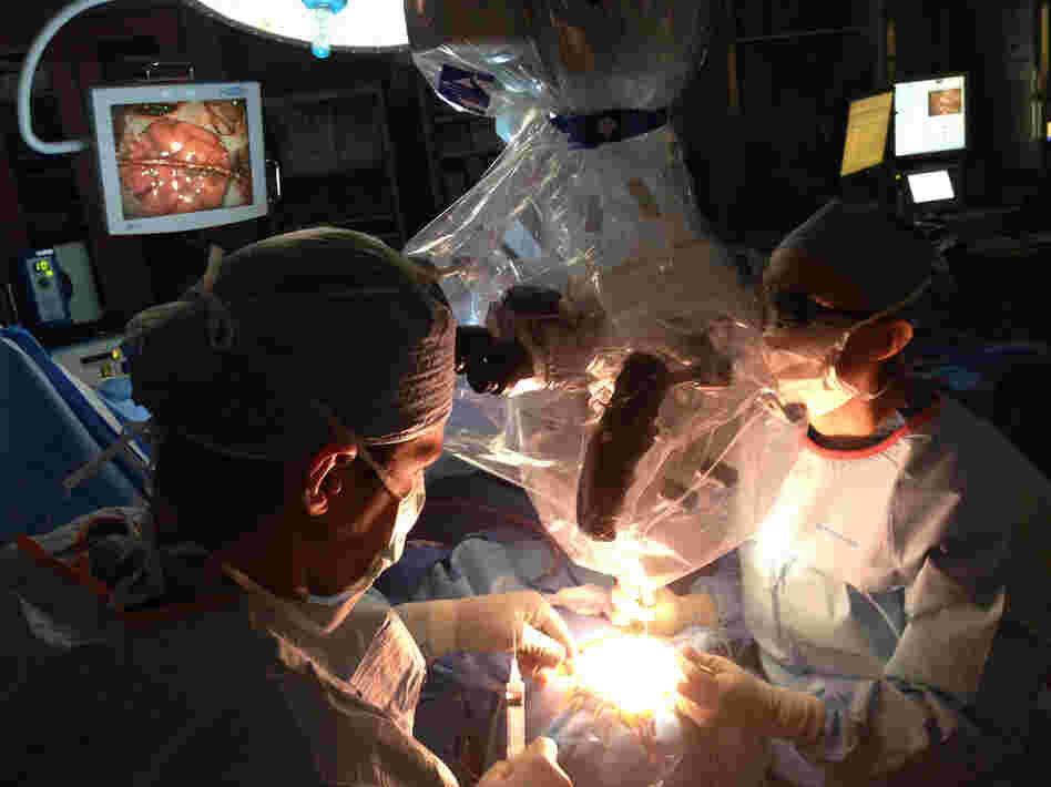 Neurosurgeons Ed Smith (left) and Sarah Jernigan operate on Maribel Ramos' brain. The monitor at upper left shows a portion of Maribel's brain, crossed by the healthy blood vessel they'll use to bring a new supply of blood to her oxygen-starved brain.