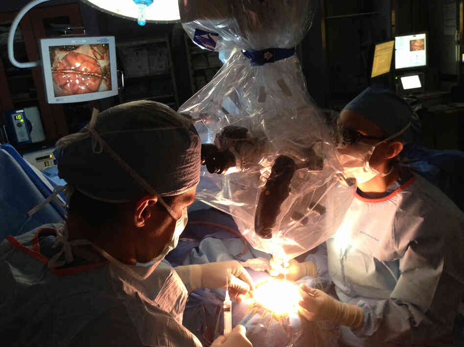 Neurosurgeons Ed Smith (left) and Sarah Jernigan operate on Maribel Ramos' brain. The monitor at upper left shows a portion of Maribel's brain, crossed by the healthy blood vessel they'll use to bring a new supply of blood to her oxygen-starved brain.