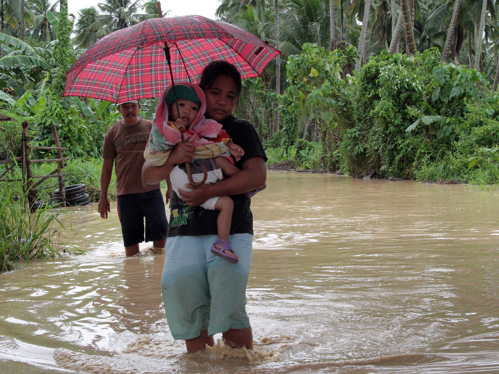 A woman carries a child through a flooded road on the island of Mindano.