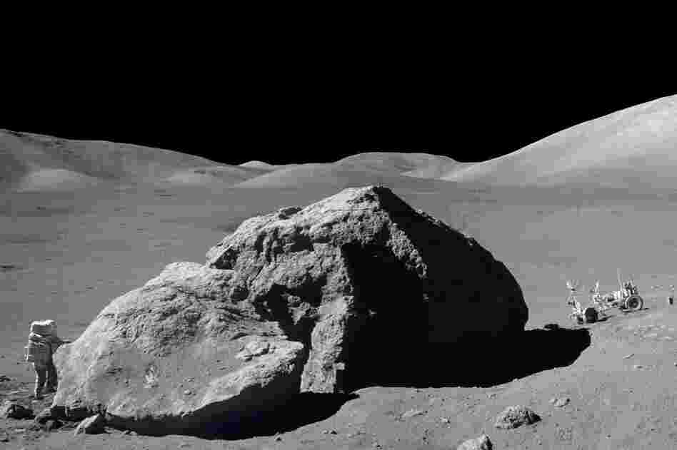 Schmitt is photographed standing next to a huge, split lunar boulder at the Taurus-Littrow landing site. The lunar roving vehicle is visible in the background. This photo is made from two frames from one of Apollo 17's cameras.
