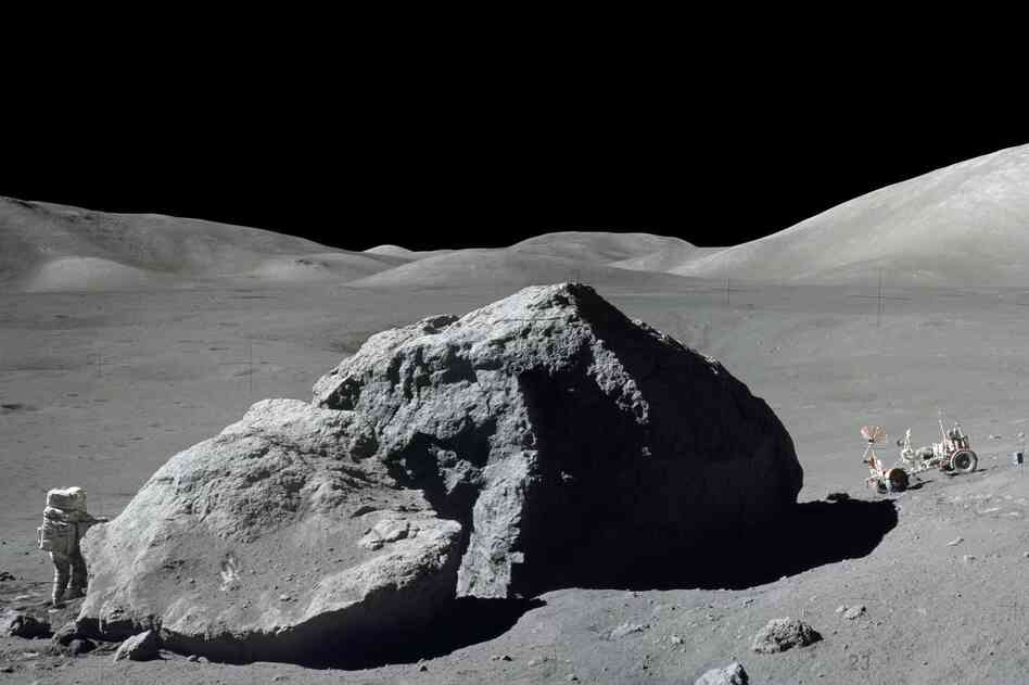 Schmitt is photographed standing next to a huge, split lunar boulder at the Taurus-Littrow landing site. The lunar roving vehicle is visible in the background. This photo is made from two frames from one of Apollo 17's cameras.