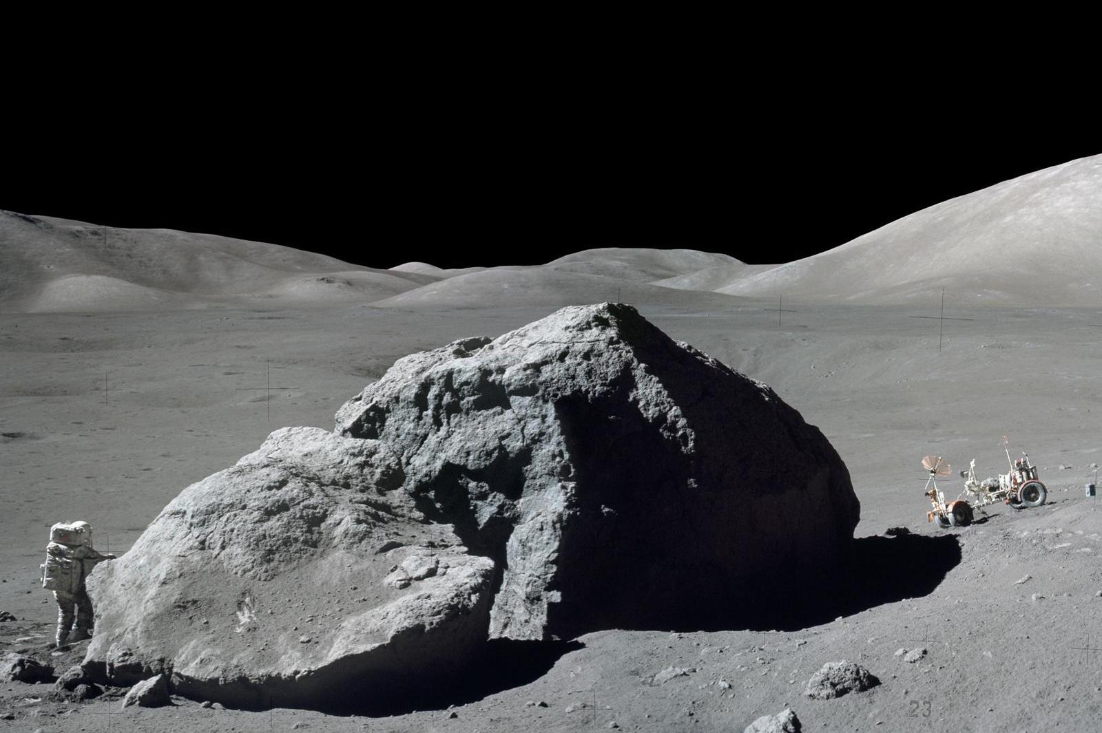 Schmitt is photographed standing next to a huge, split lunar boulder at the Taurus-Littrow landing site. The lunar roving vehicle is visible in the background. This photo is made from two frames from one of Apollo 17's cameras.