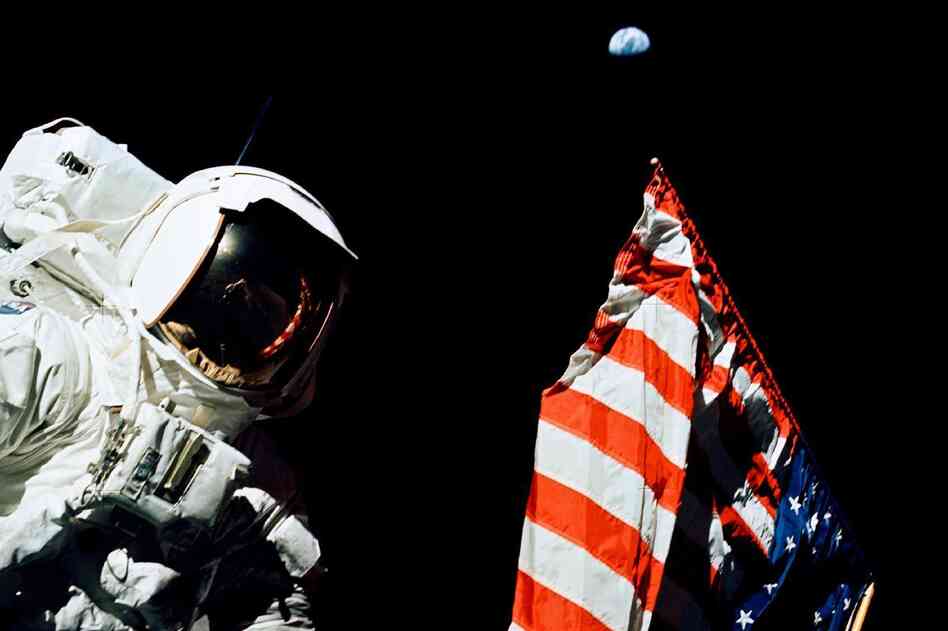 Schmitt stands by the American flag during a moonwalk. Look above the flag — that's Earth, a quarter-million miles away.