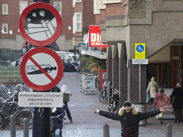 A young man with a joint in his left hand jokes with the photographer as he passes a sign prohibiting the use of marijuana and alcohol, in a designated area in Amsterdam on Wednesday. The city's mayor says students would be formally banned from smoking marijuana at school as of Jan. 1, 2013.