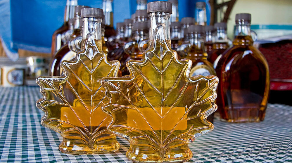 Fresh maple syrup in two maple leaf-shaped bottles, with other bottles behind. Police officials have arrested three men who allegedly siphoned the sweet treat from 16,000 storage barrels stored in a Quebec warehouse.