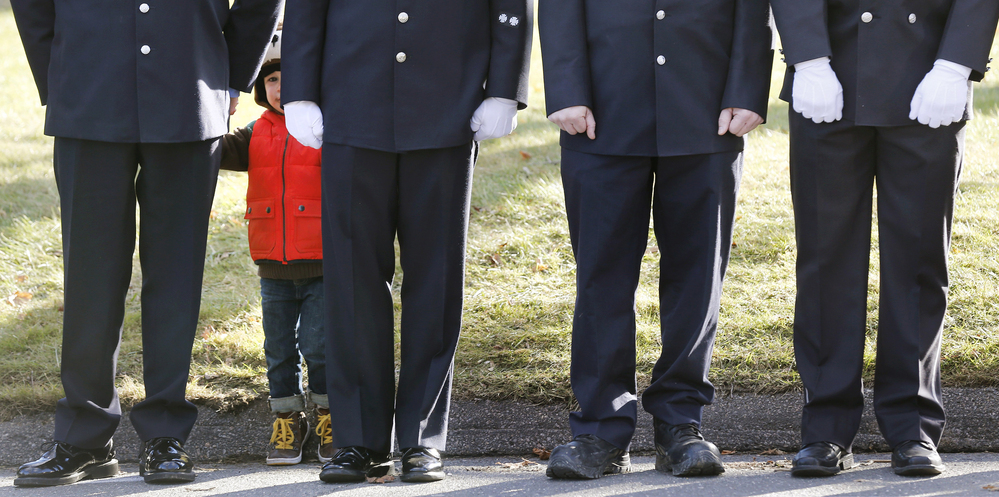 A child peers through firefighters standing as the procession heads to the cemetery outside the funeral for school shooting victim Daniel Barden at St. Rose of Lima Catholic Church in Newtown, Conn.,