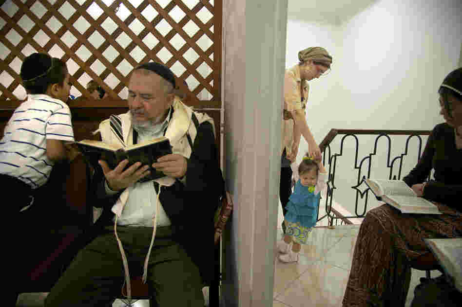 A man reads from a prayer book while a mother cares for her daughter during prayers at Bello's synagogue.