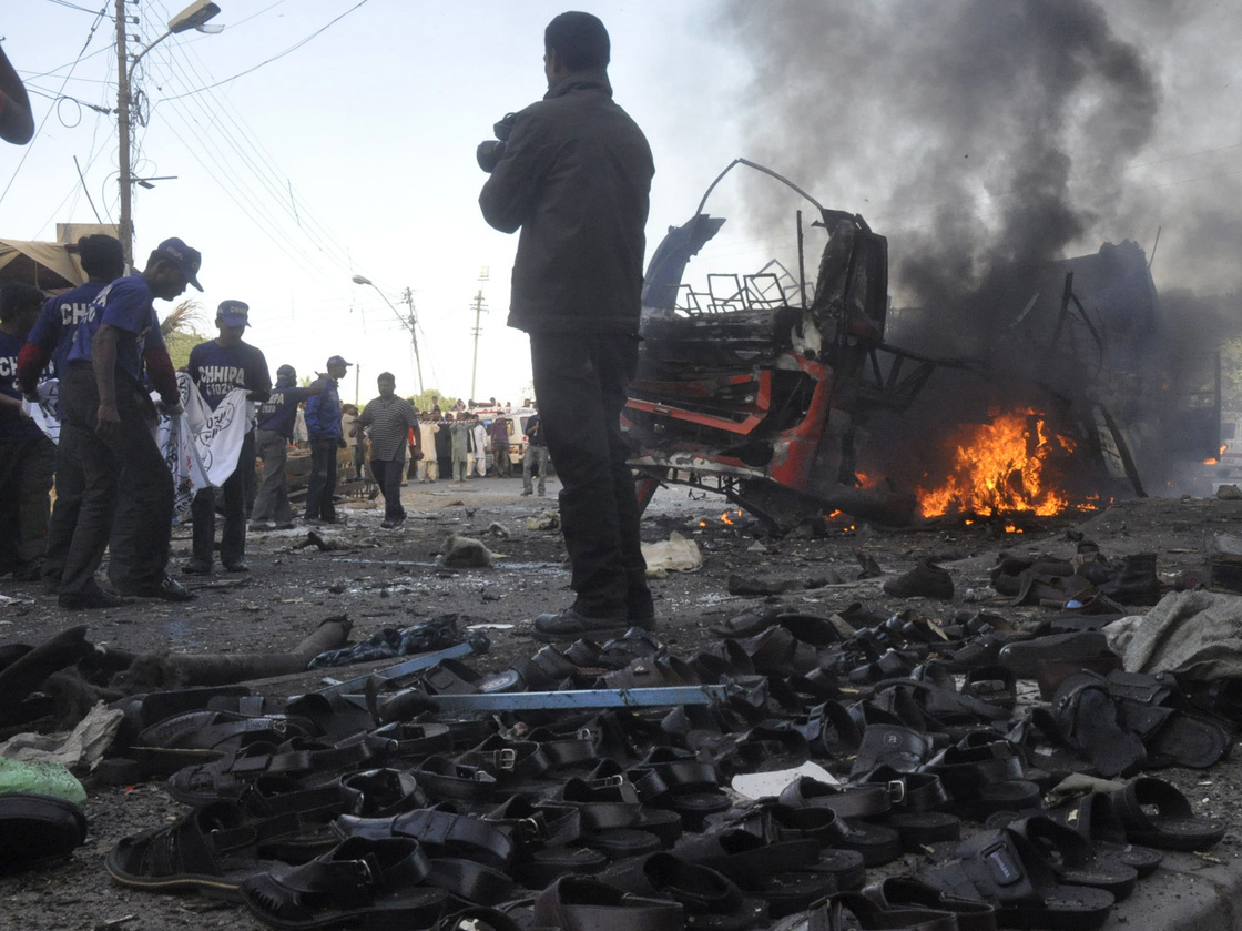 Rescuers carry a sheet to collect body parts near the scene of a bomb explosion in Karachi on Saturday that killed at least six people and . wounded 48. The sandals in the foreground are displayed for sale.