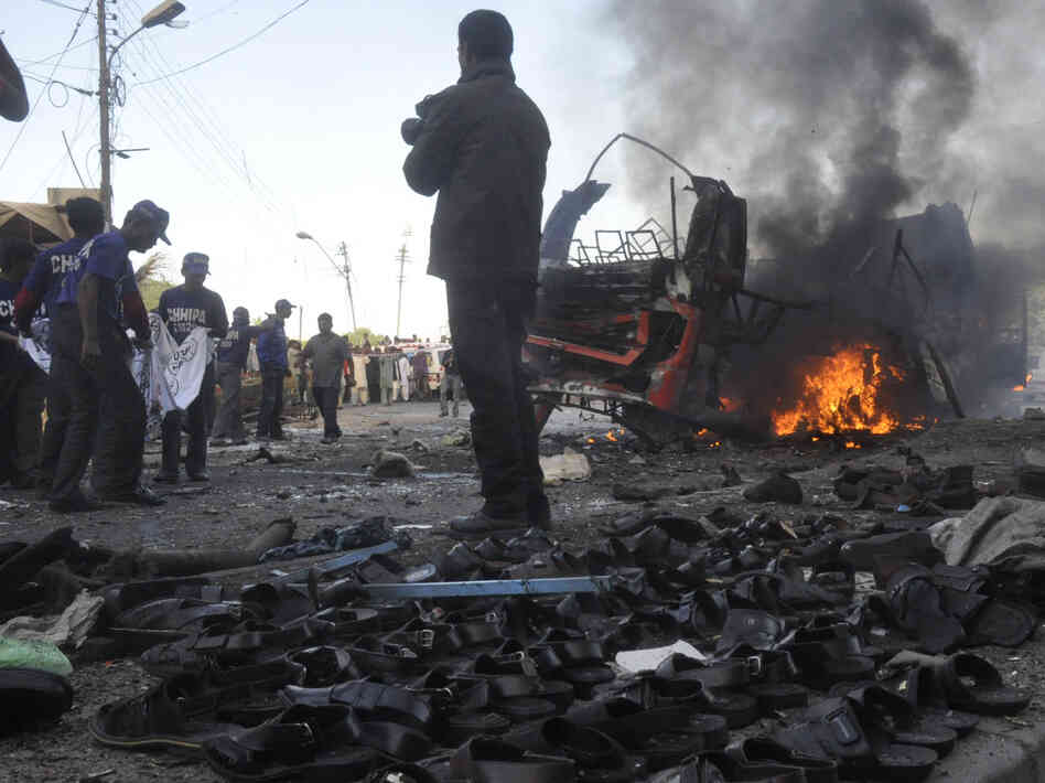Rescuers carry a sheet to collect body parts near the scene of a bomb explosion in Karachi on Saturday that killed at least six people and . wounded 48. The sandals in the foreground are displayed for sale.