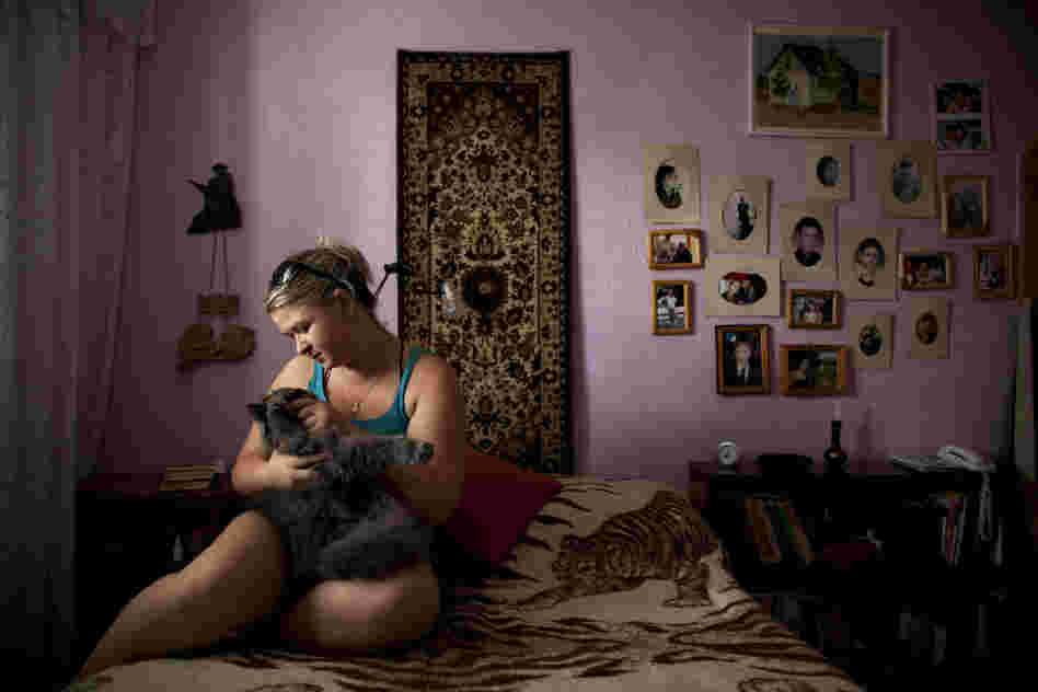 Alexandra Bahman, who immigrated to Israel from Moldova in 2006, sits in her bedroom with her cat in Ashdod. Bahman left Moldova with the carpet and photos that now decorate her bedroom walls.