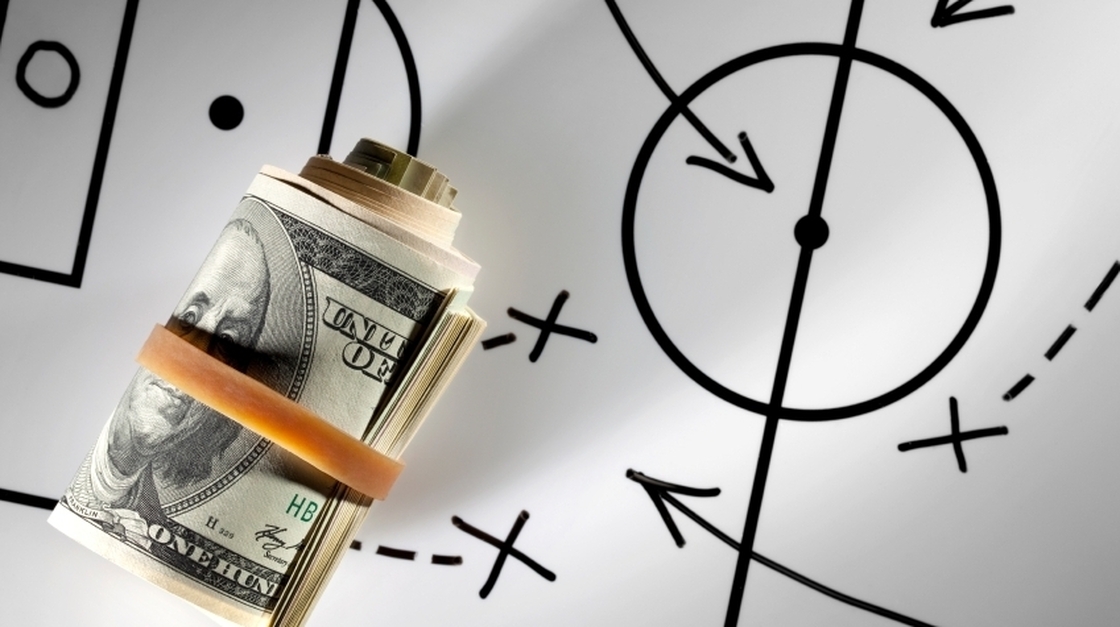 Roll of dollars on a blackboard with football strategy planning.