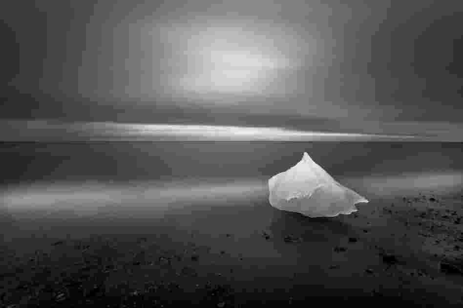 "Glacial ice washes ashore after calving off [a] glacier on Iceland's eastern coast. During the waning light of summer this image was created over the course of a 4-minute exposure while the photographer backlit the grounded glacial ice with a headlamp for 2 of those 4 minutes."