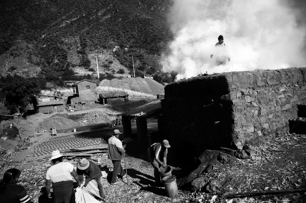 Carlos Apasa (in smoke) and his family tend to their traditional oven as they fire handmade roofing tiles in the village of Pinipampa. The village supplies tiles for construction projects throughout the Cusco department, and the highway has made transport much faster and easier.