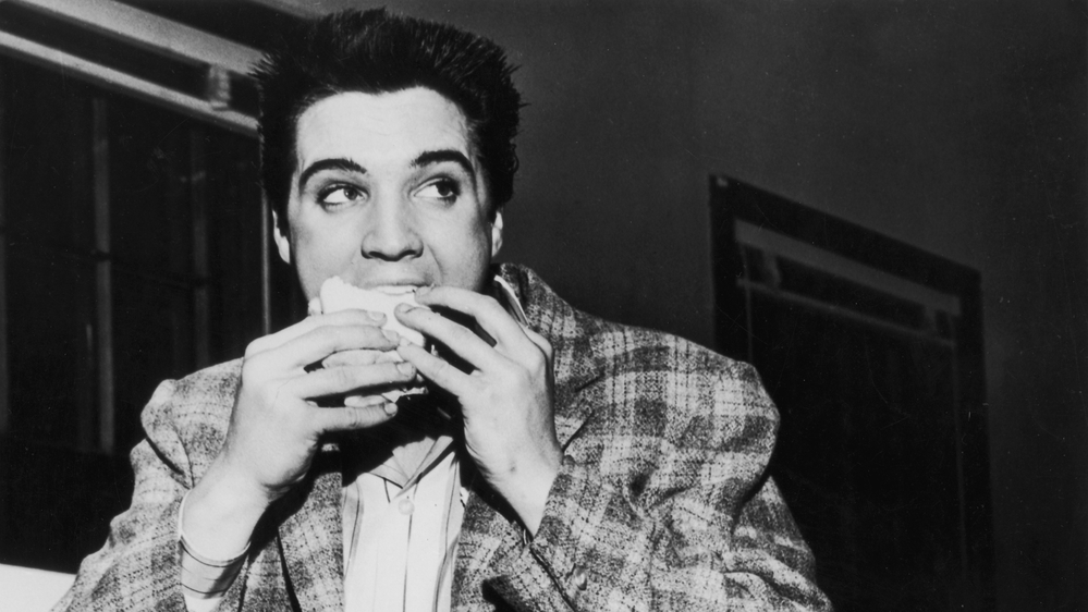 A still-trim Elvis Presley enjoys a sandwich in 1958. His love of fatty foods hadn't caught up to him yet.
