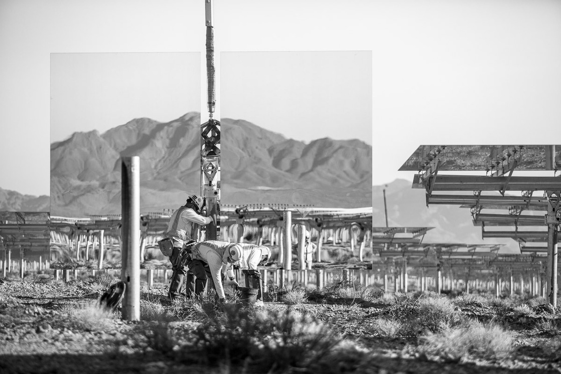 Workers install a "heliostat" — or a device with a mirror that reflects the sun, or in this case the nearby mountains. Background shows assembled heliostats in "safe" or resting position. June 2012.