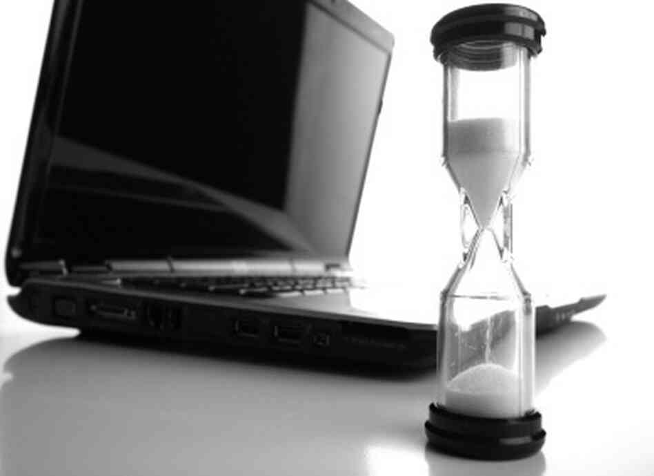 Wide angle shot of an hourglass with laptop computer in the background.