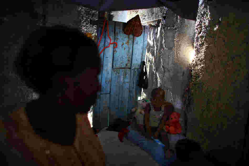 Bibeta Louissaint (left) stands in her makeshift shack with her 2-year-old son, Sebastian, in the Fort National neighborhood of Port-au-Prince. This area was home to many people living in the camps around the national palace. Louissaint received a rental subsidy last year to move.