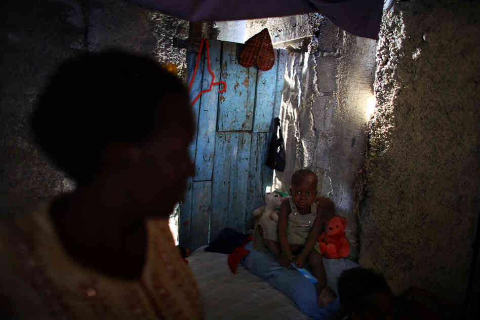 Bibeta Louissaint (left) stands in her makeshift shack with her 2-year-old son, Sebastian, in the Fort National neighborhood of Port-au-Prince. This area was home to many people living in the camps around the national palace. Louissaint received a rental subsidy last year to move.