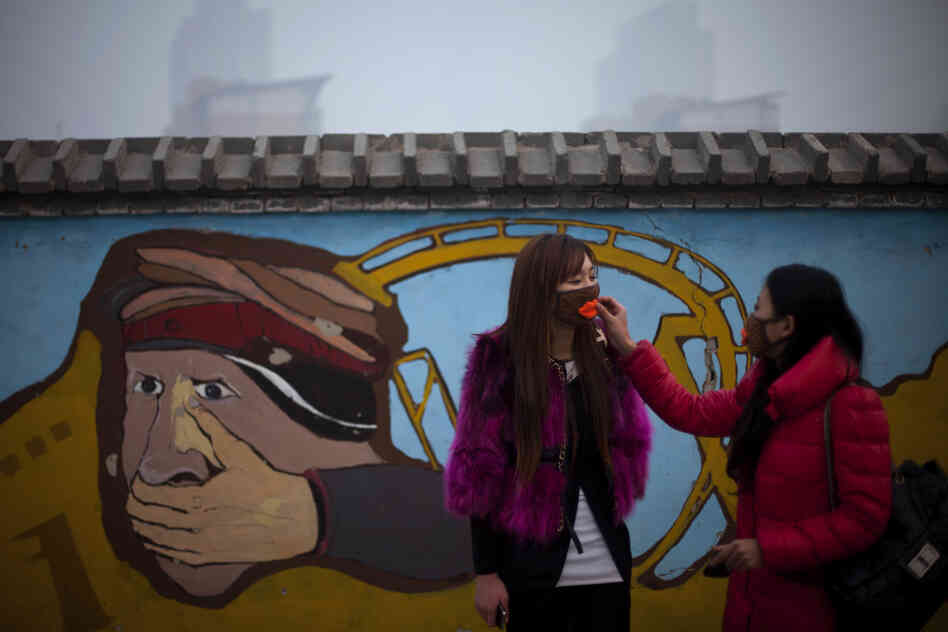 A woman helps adjust a mask for her friend outside an amusement park on a hazy day in Beijing on Saturday.