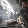 A man makes bread as residents, background, stand in line in front of a bakery during heavy fighting between Free Syrian Army fighters and government forces in Aleppo, Syria, on Dec. 4, 2012.