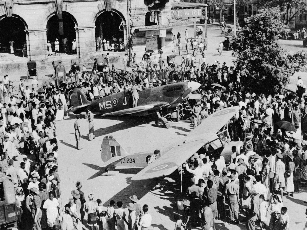 A crowd surrounds a British Spitfire and an Auster in the courtyard of the Civic Hall in Rangoon, Burma, on April 3, 1946.