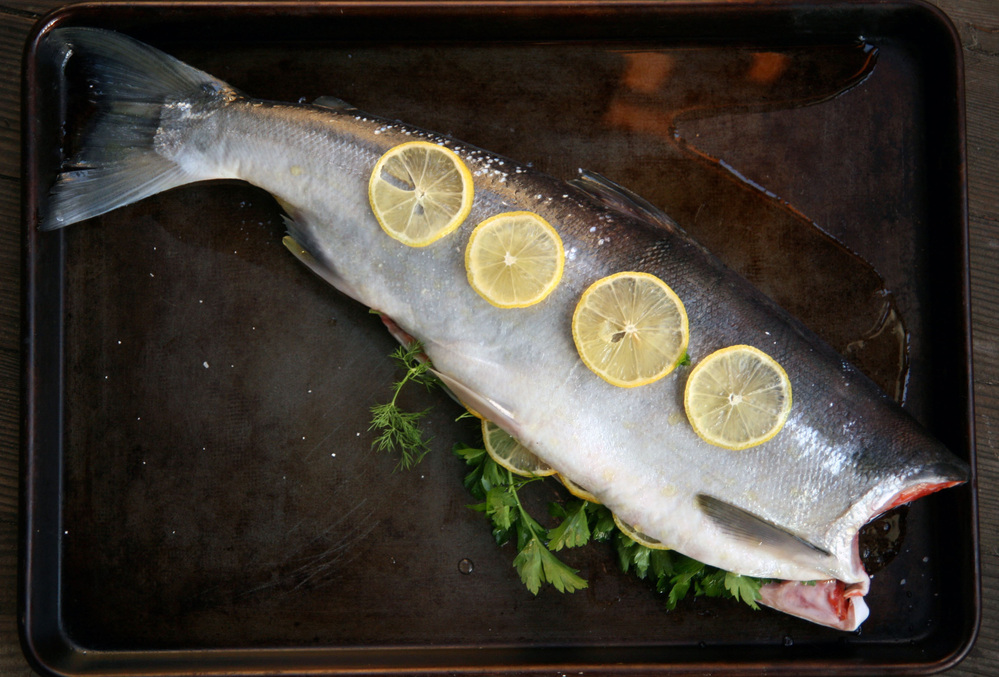 The Roasted Whole Salmon is prepped for the oven with lemon slices inside and out, plus fresh herbs and spices.