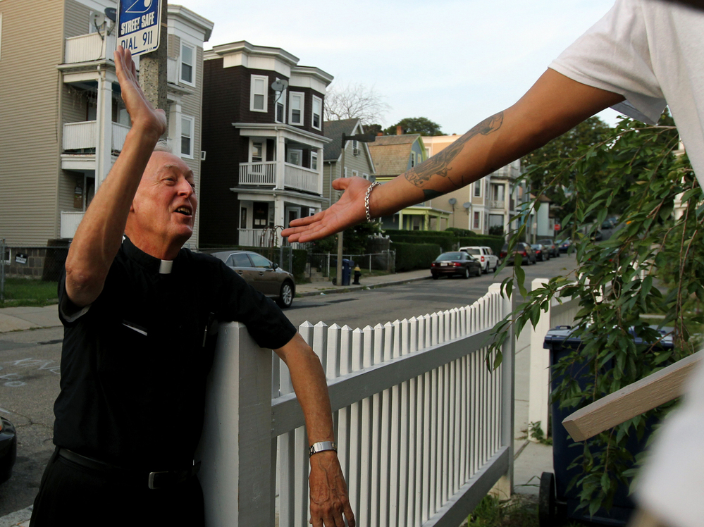 Father Richard "Doc" Conway, of St. Peter Church, high-fives a man while walking the neighborhood on a Friday night.