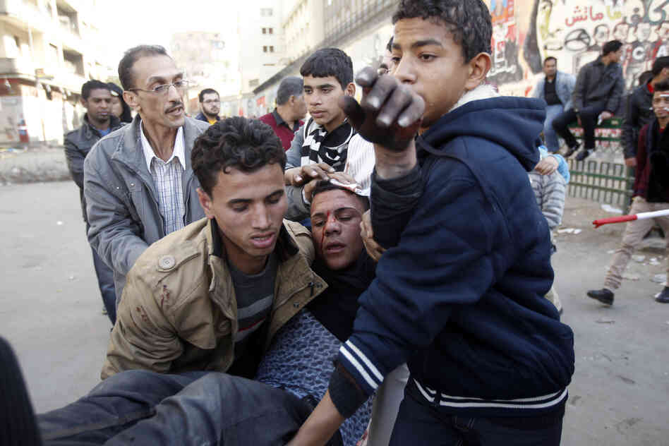 Egyptians carry a wounded protestor during clashes with riot police in Tahrir Square on January 25, 2013. 