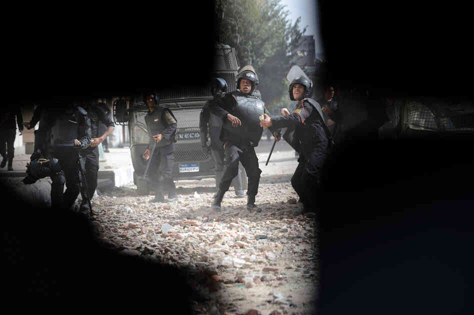 Egyptian security forces are seen through a hold in the wall, as they throw stones at protesters in Sheikh Rayhan street, that leads to the Interior Ministry headquarters, near Tahrir Square, on January 25, 2013. 
