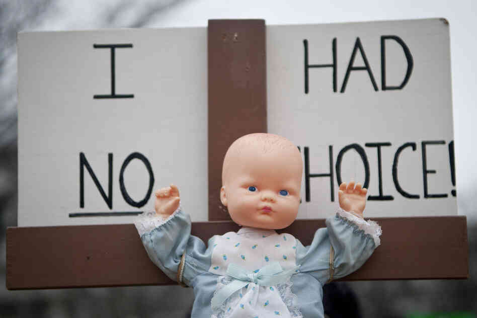 A toy baby doll is crucified on a cross.