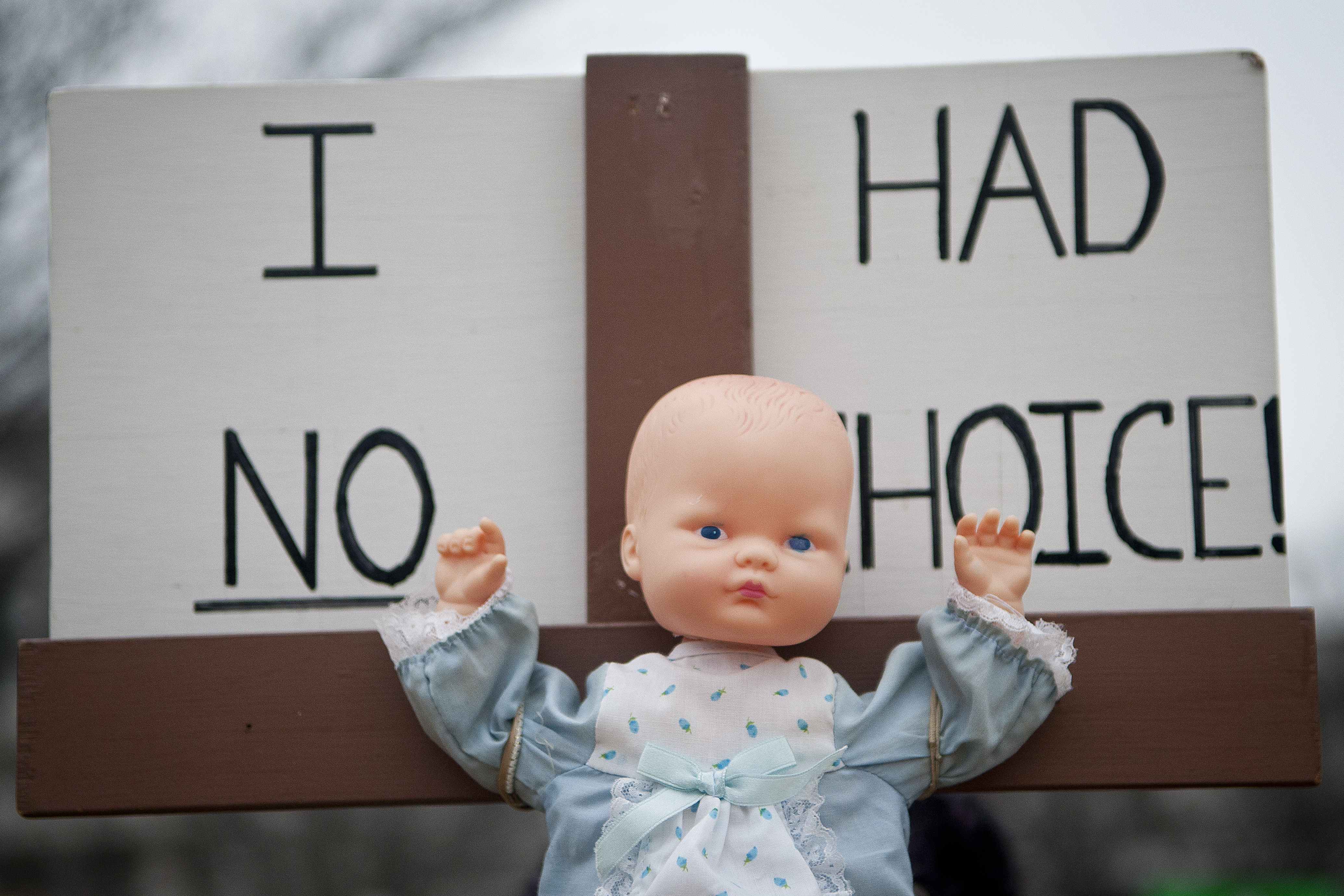 A toy baby doll is crucified on a cross.