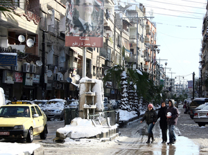 Damascus residents still get out during the day, but the streets empty at night. Here, Damascenes walk past a poster of President Bashar Assad on Jan. 10, following a heavy snow.