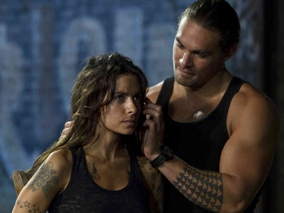 Sarah Shahi's tattoo artist — who has ties to both Kang and Stallone's characters — falls into the clutches of a mob enforcer (Jason Momoa).