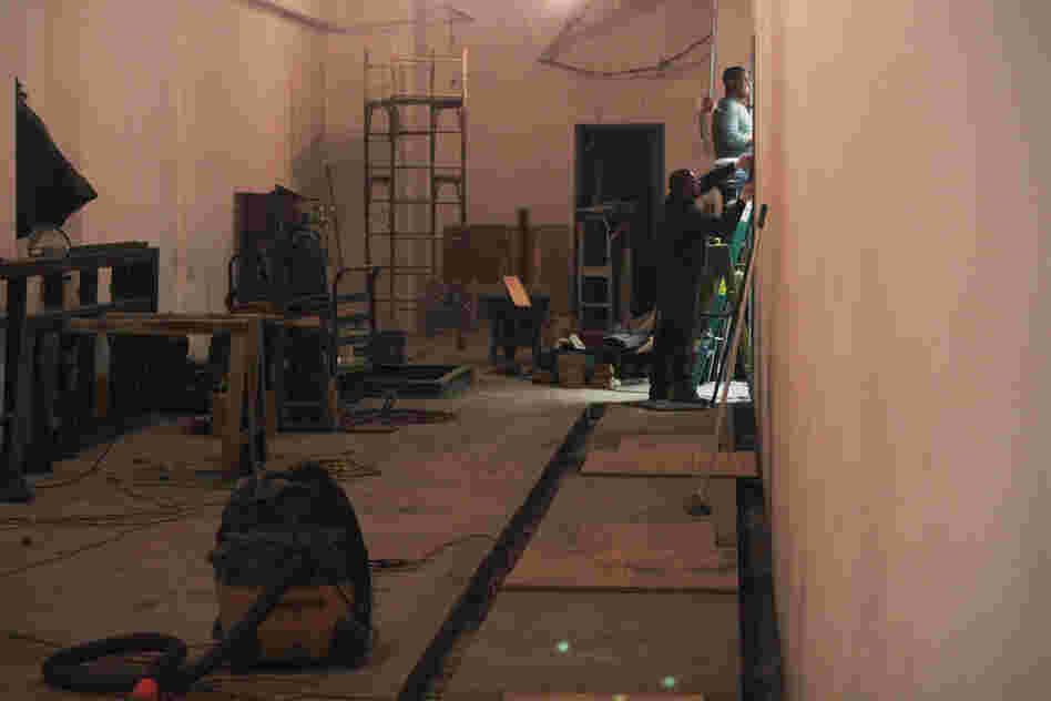 Workers on the main floor close off a former eyeglass store as they prepare to install electrical switching equipment.