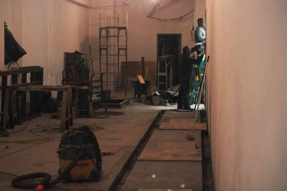 Workers on the main floor close off a former eyeglass store as they prepare to install electrical switching equipment.