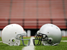 Two football helmets face each other on a field. Two football helmets face each other on a field.