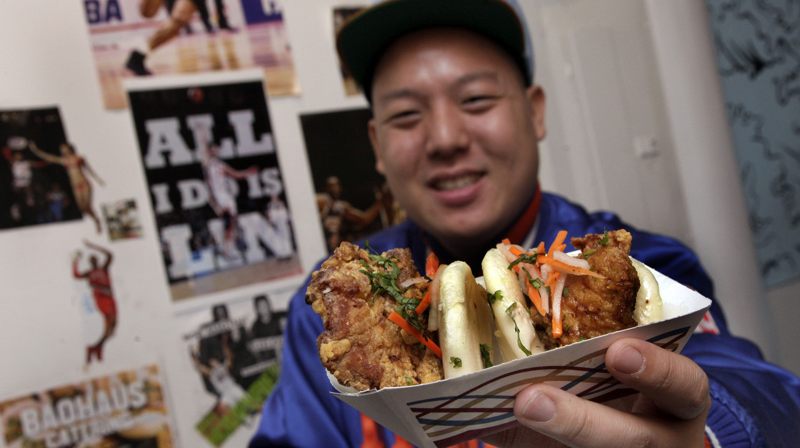 Eddie Huang, co-owner of Baohaus and author of Fresh Off The Boat, holds a pair of "The Taiwanese Te-Bao," a Taiwanese pork chop with curry seasoning, pickles daikon-carrot, jalapeno, aioli and cilantro in a steamed bun.