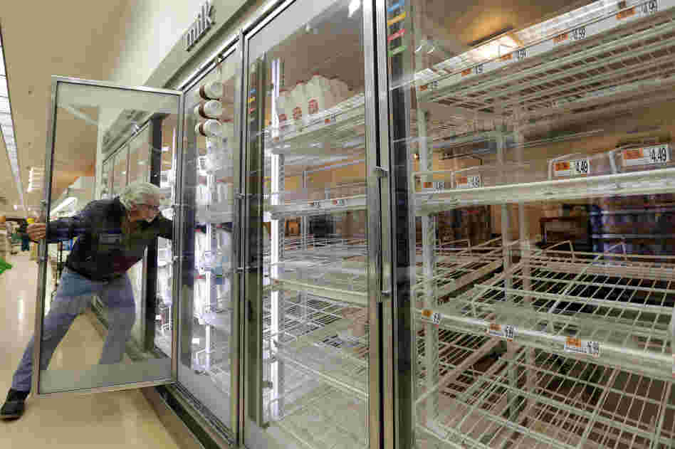 Jack Percoco reaches into depleted shelves for milk at a supermarket in Somerville, Mass.