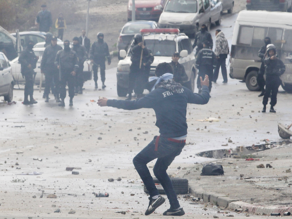 A protester, and riot police in the background, during the clashes Friday in Tunis.