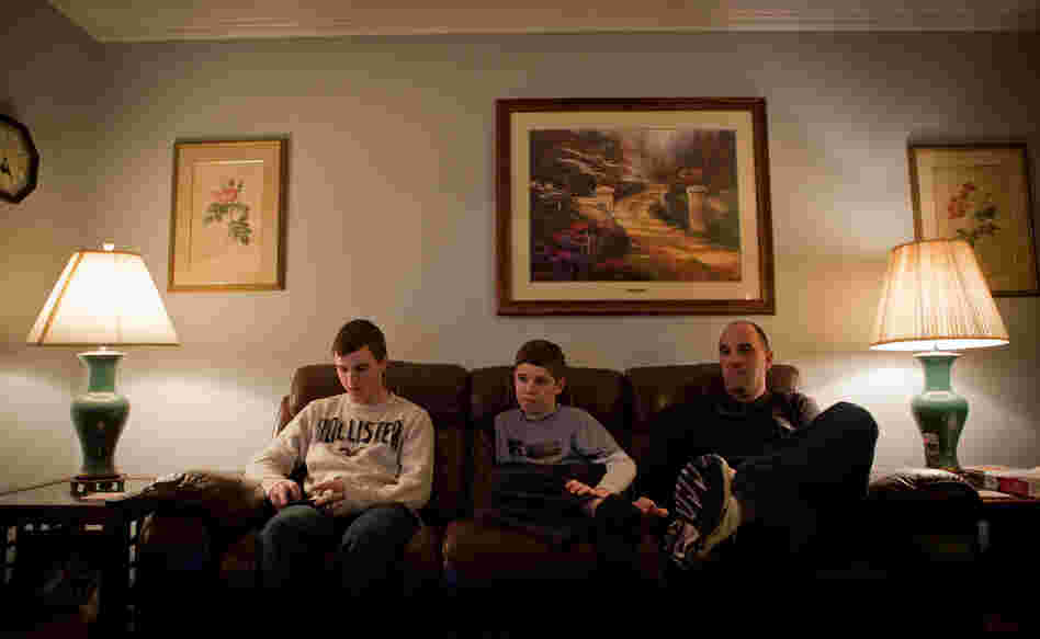 Brian Jordan checks his iPhone while Kevin and their father watch television. Brian Jordan checks his iPhone while Kevin and their father watch television.