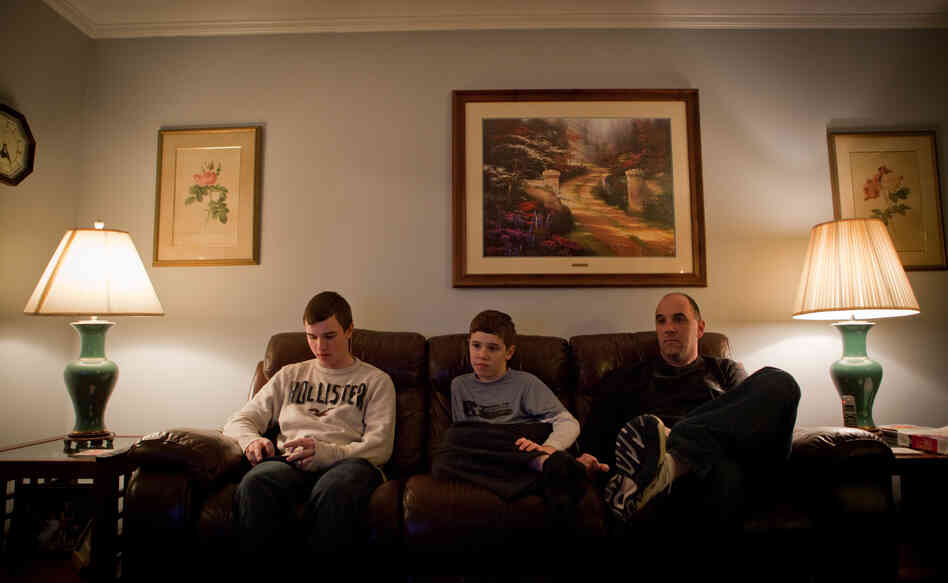 Brian Jordan checks his iPhone while Kevin and their father watch television. Brian Jordan checks his iPhone while Kevin and their father watch television.