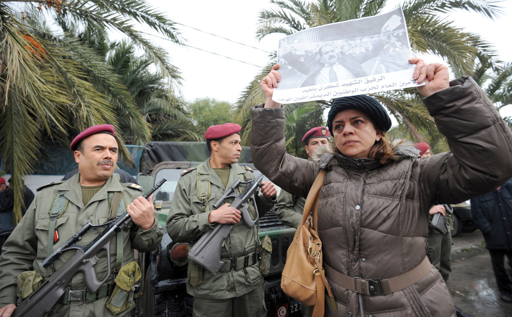 Tunisian soldiers stand guard as a woman holds up a poster featuring opposition leader Chokri Belaid during his funeral procession in a suburb of Tunis on Feb. 8. Belaid's assassination has laid bare the political rifts in post-revolutionary Tunisia.