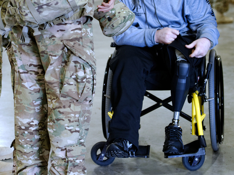 While his unit waits for buses to take them to a gym where family and friends will greet them, Jeffries sits in a wheelchair, one of his prosthetic legs visible.