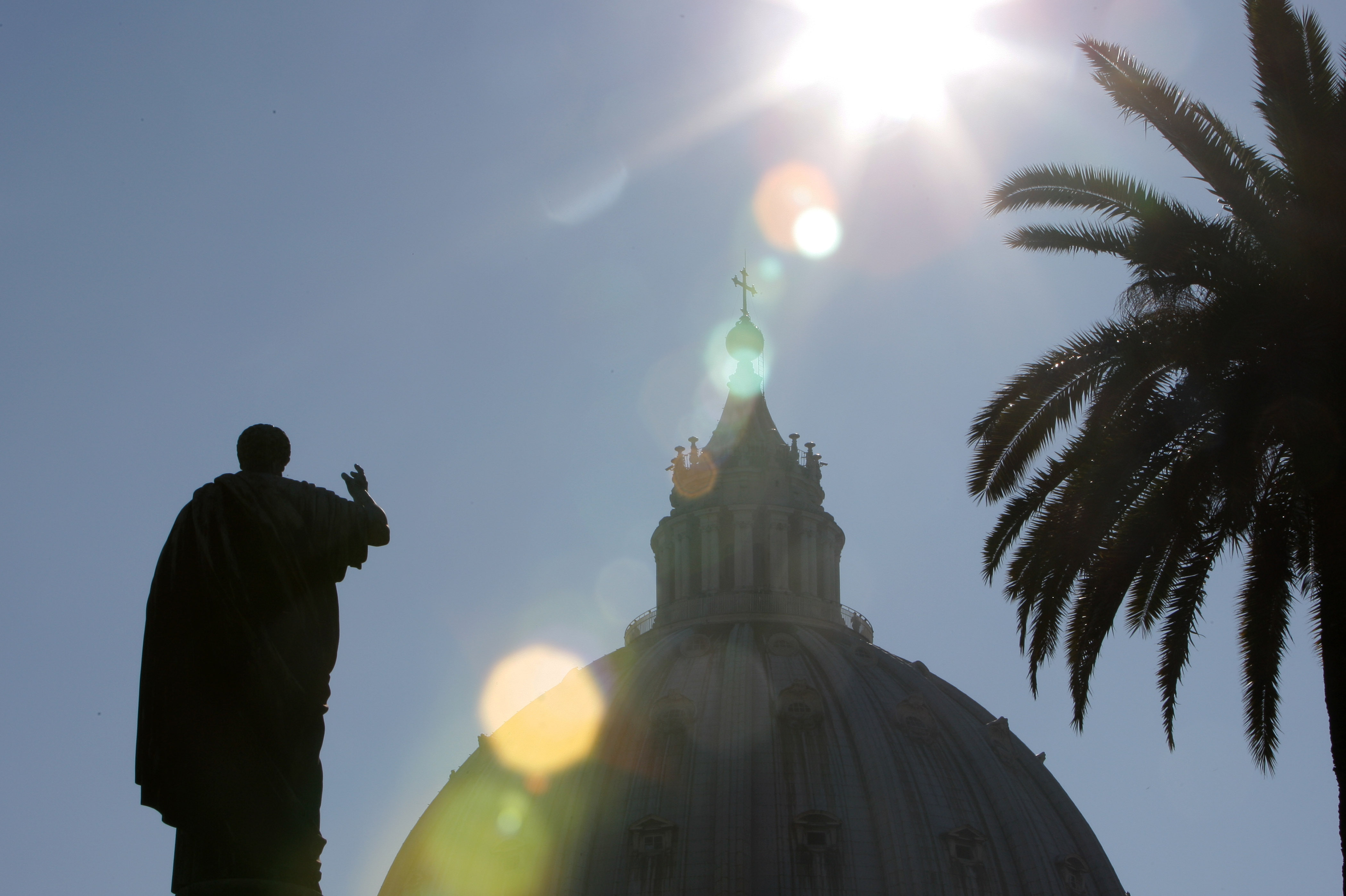A silhouette of St. Peter's statue in front of St. Peter's Basilica is seen from the Vatican Gardens.