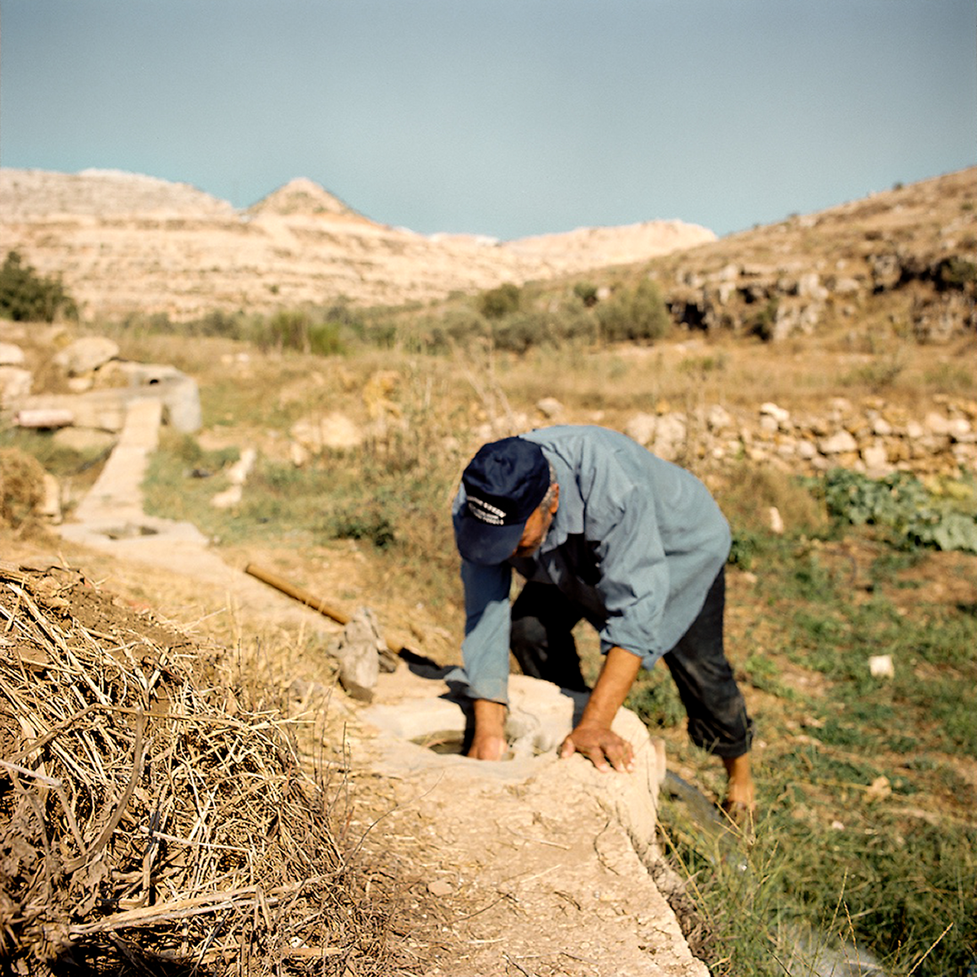 Jamil is treating the ancient canal, letting the water flow to his fields. The ruined landscape in the background is a result of quarrying stones for the settlement construction.
